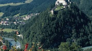 A castle on a hill with a valley and mountains in the background.
