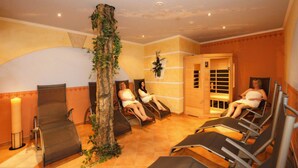 Een wellnessruimte met ligstoelen, een grote boomstam met klimplanten en een houten sauna deur.