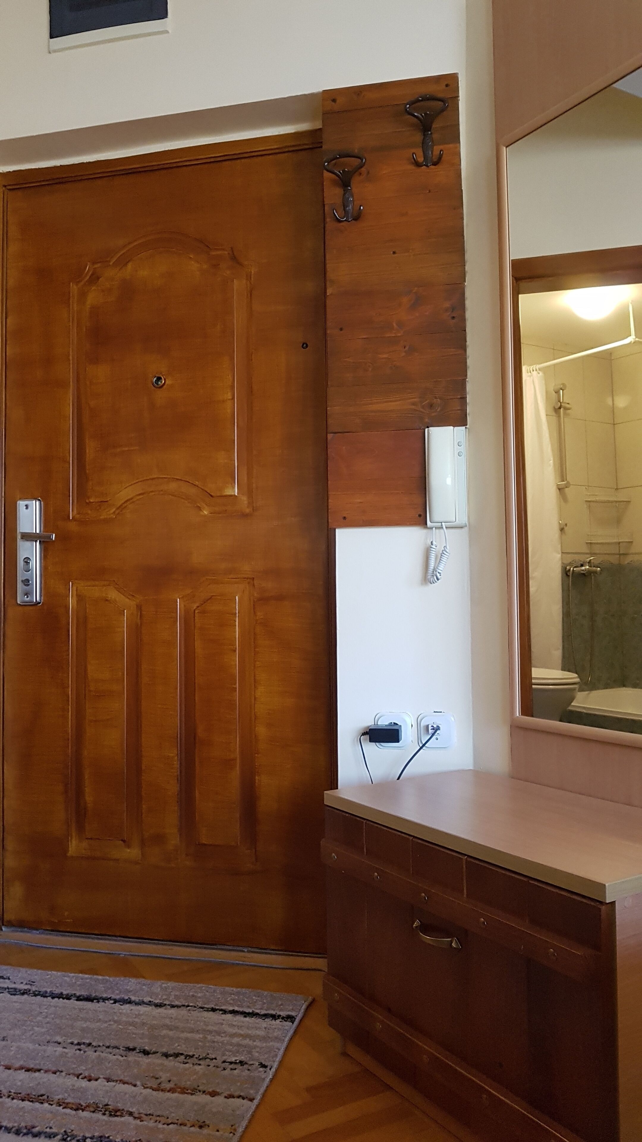 Una puerta de madera con manija, un espejo sobre un tocador con lavamanos y una ducha visible a través de una puerta de vidrio.