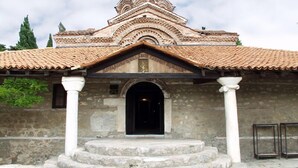 Un edificio con techo de tejas, entrada central y columnas de piedra.