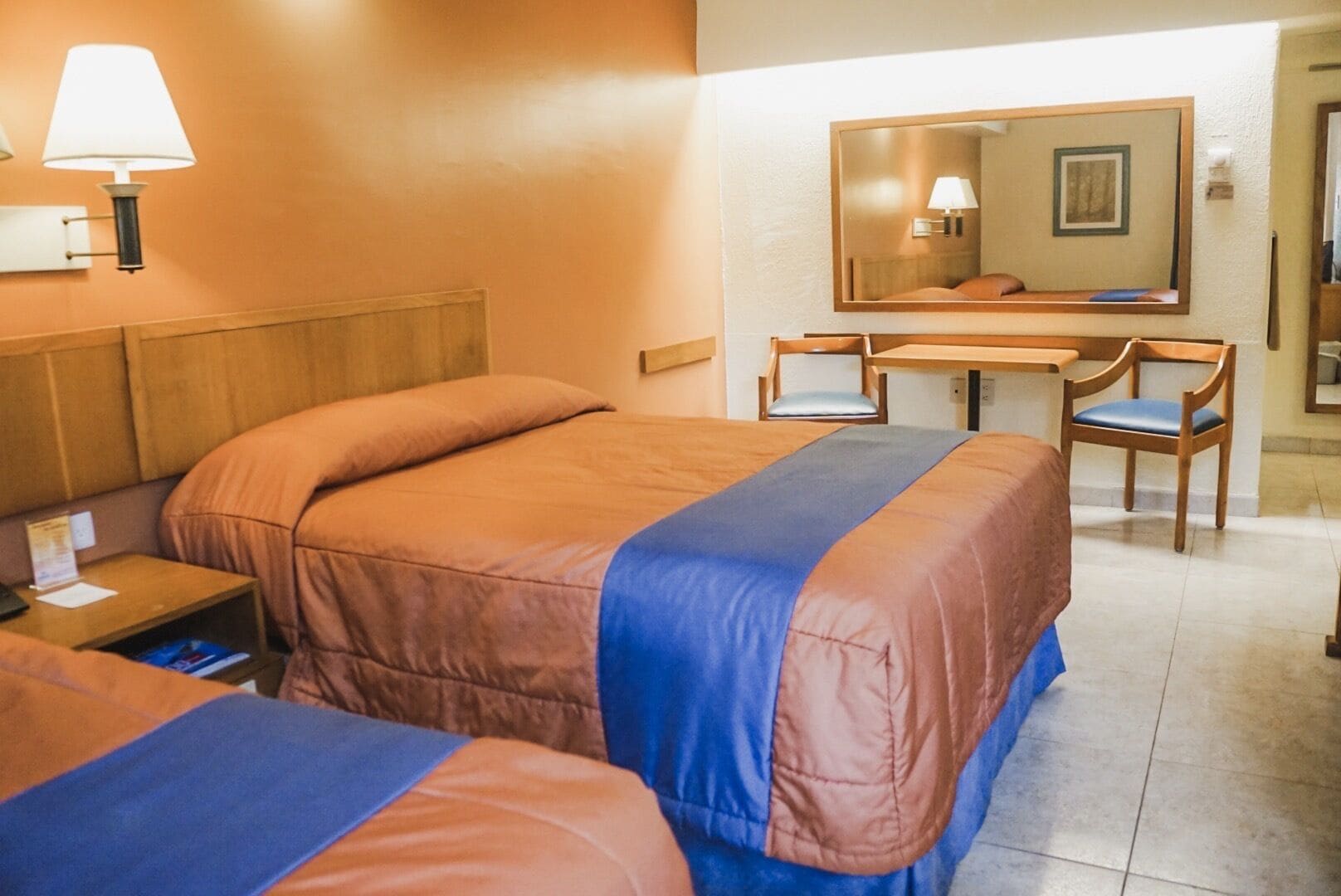 A hotel room with two beds, a desk, a chair, and a mirror.