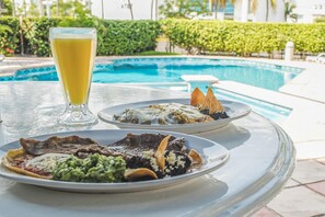 A dining table with two plates of food and a glass of orange juice near a swimming pool. - Hotel Jaragua (Boca del Río)