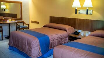 Habitación de hotel con dos camas, un escritorio con una silla, un espejo y dos lámparas de pared.