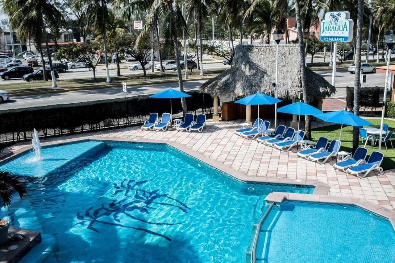 A swimming pool with lounge chairs and umbrellas, surrounded by palm trees and a restaurant sign.