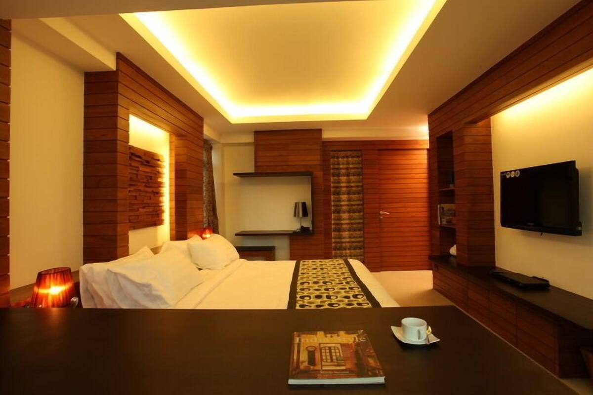 Una habitación de hotel con cama, mesita de noche, lámpara, televisor y paneles de madera.