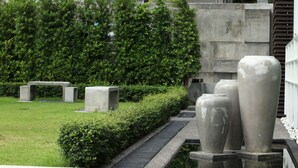 Een tuin met een pad, betonnen banken en grote vazen.