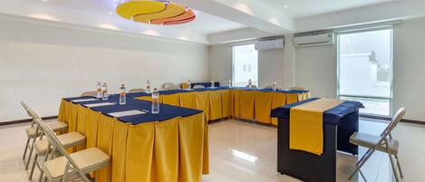 Un salón de conferencias con mesas cubiertas con manteles amarillos, equipado con botellas de agua y sillas.
