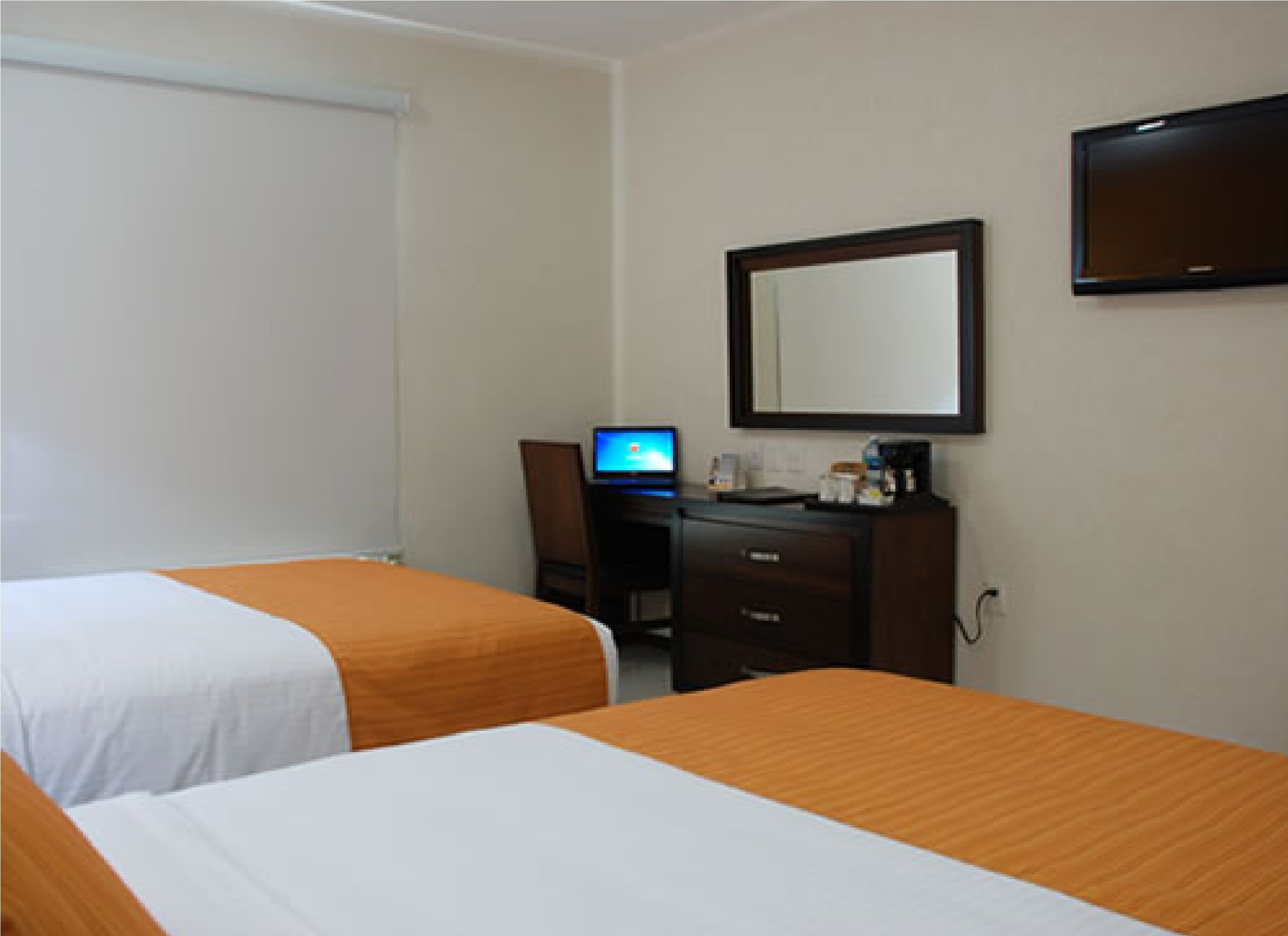 A hotel room with two beds, a desk with a computer, a mirror, and a television.