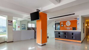 Egy modern dizájnnal megtervezett szállodai recepciós tér, melyben található egy recepciós pult, egy síkképernyős televízió és egy „Comfort Inn” feliratú tábla.