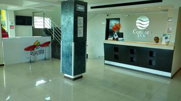 A hotel reception area with a modern design, including a reception desk, a staircase, and a 'Top Tours' sign.