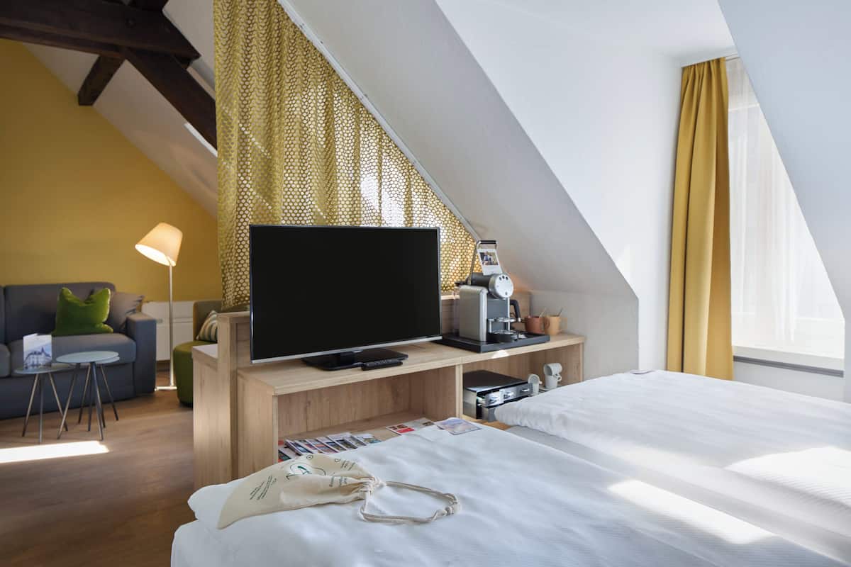 A hotel room with a TV, bedside table, lamp, and a bed.