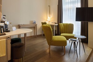 Moderni hotellihuone, jossa on työpöytä, kaksi tuolia, pieni pöytä, lamppu ja televisio.