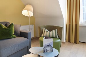 Una habitación moderna con un sofá, un sillón verde, una mesita redonda y una lámpara.