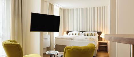 A hotel room with a bed, a TV mounted on the wall, and two yellow chairs.