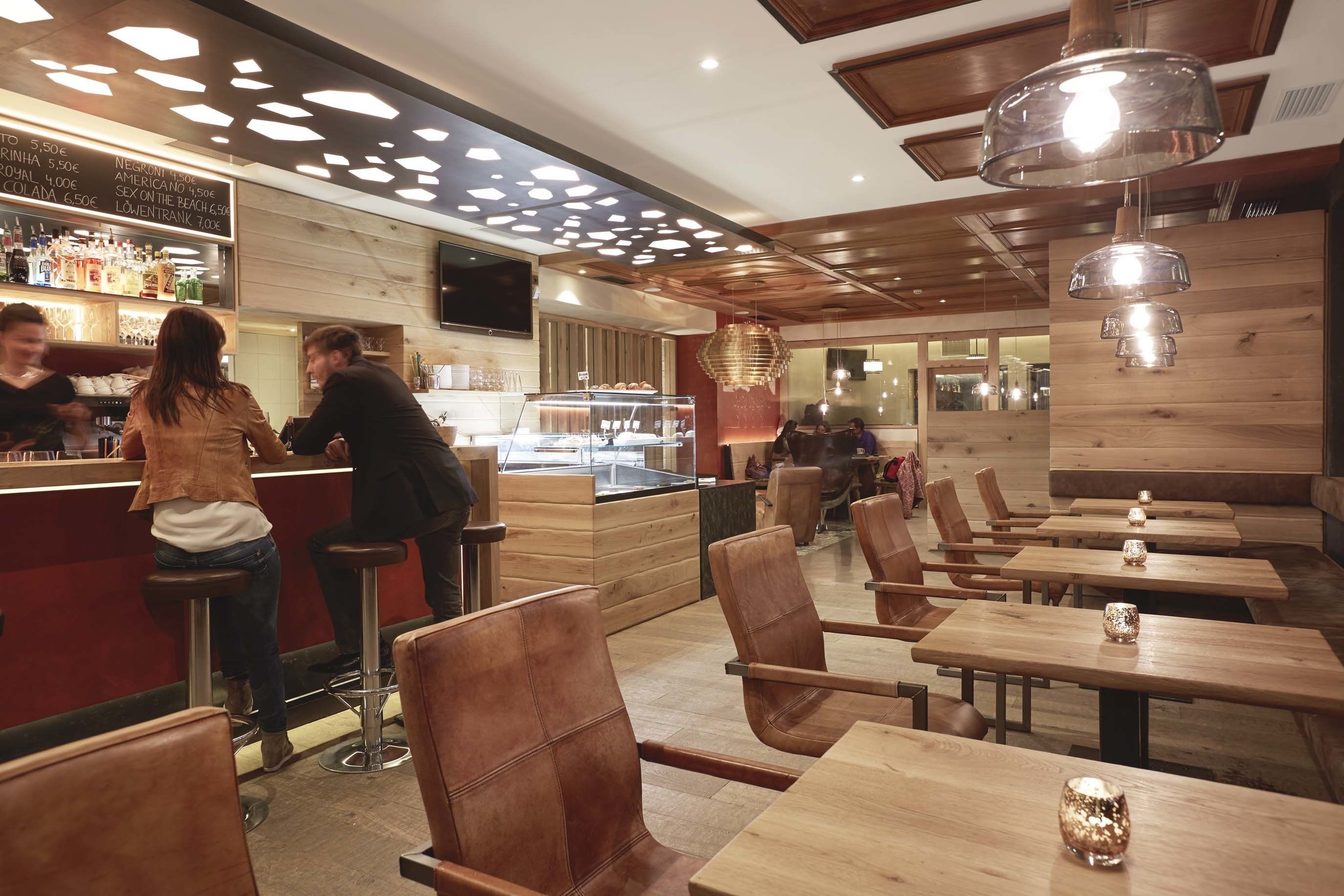 Un interior de restaurante con mesas y sillas de madera, una zona de bar y un tablero de menú que muestra precios.