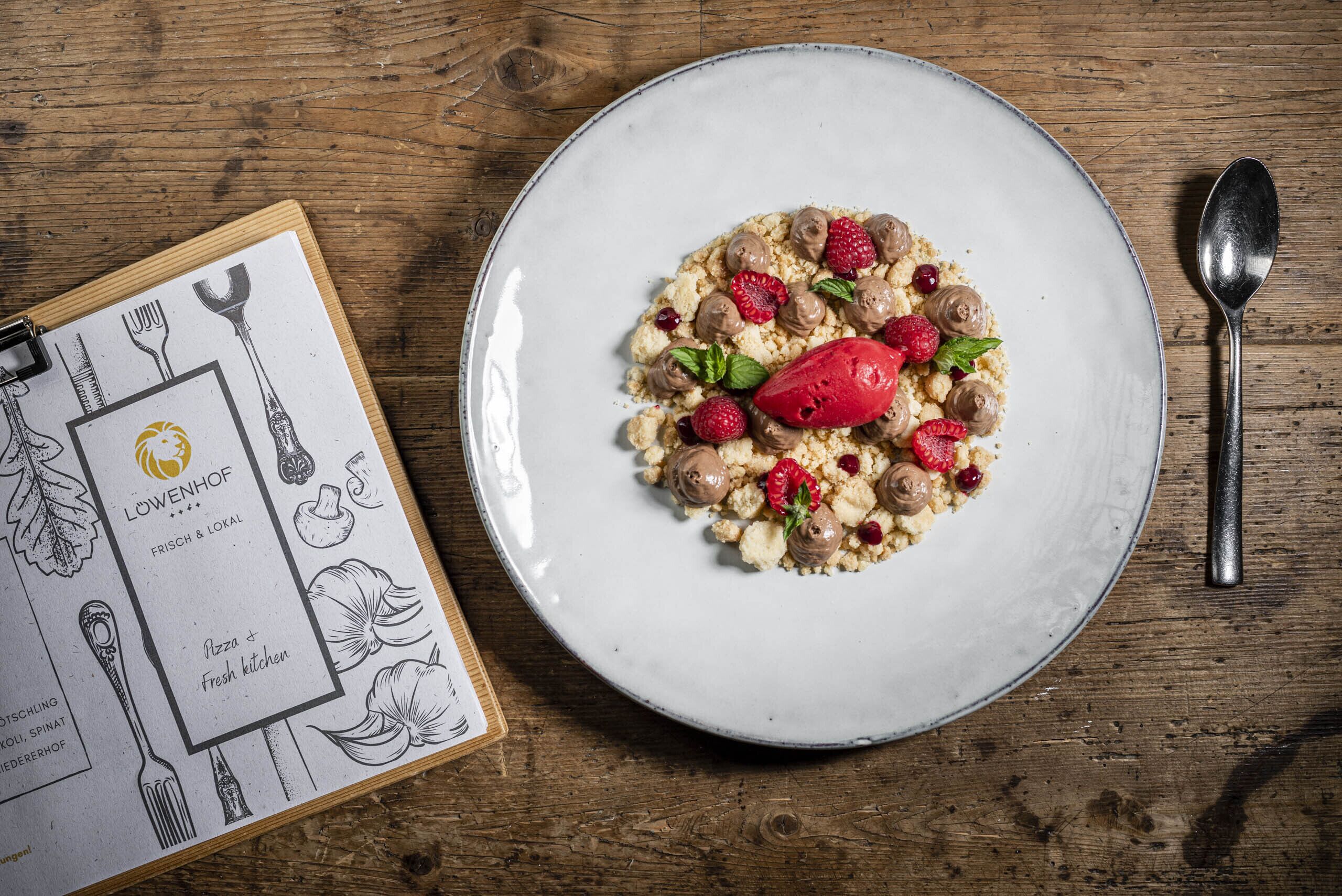 A plate of food with a spoon and a menu on a wooden table.