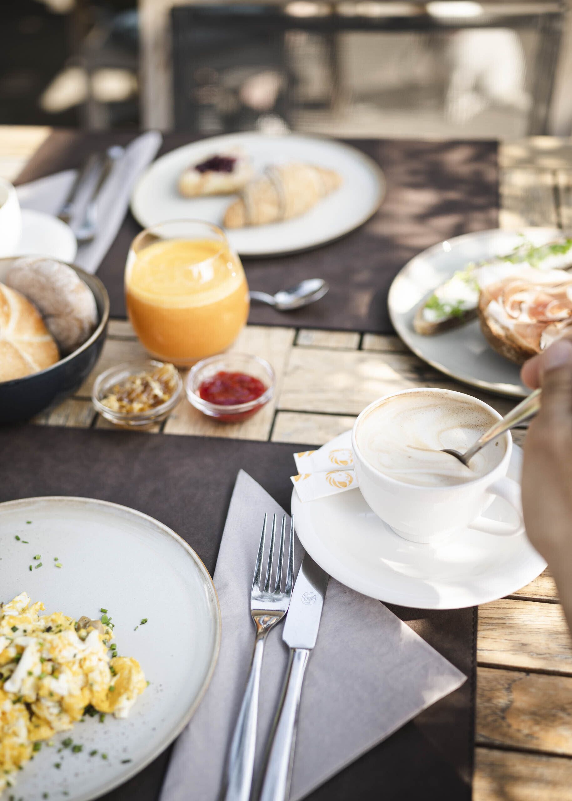 Een tafel met ontbijtproducten, waaronder roerei, een croissant en een kop koffie.