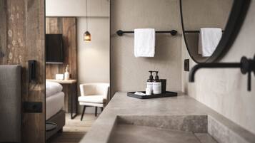 A modern bathroom with a wooden accent wall, a large mirror, and a bedside table with toiletries.