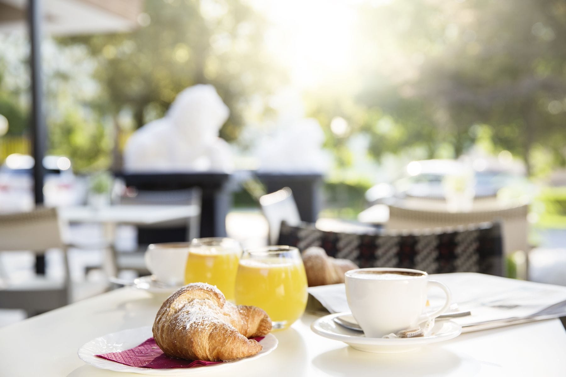 Une table dressée pour le petit-déjeuner, avec des croissants, du jus d’orange et du café.