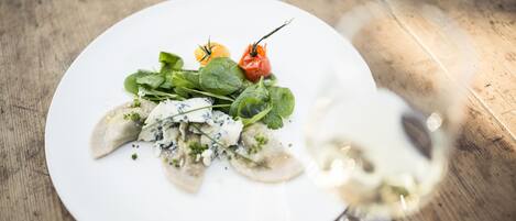 A white plate with a dish of dumplings, greens, and a red pepper on a wooden table.