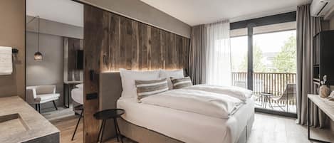 Moderni hotellihuone, jossa on suuri sänky, pieni työpöytä, tuoli ja parveke, jolta on näkymä ulos.