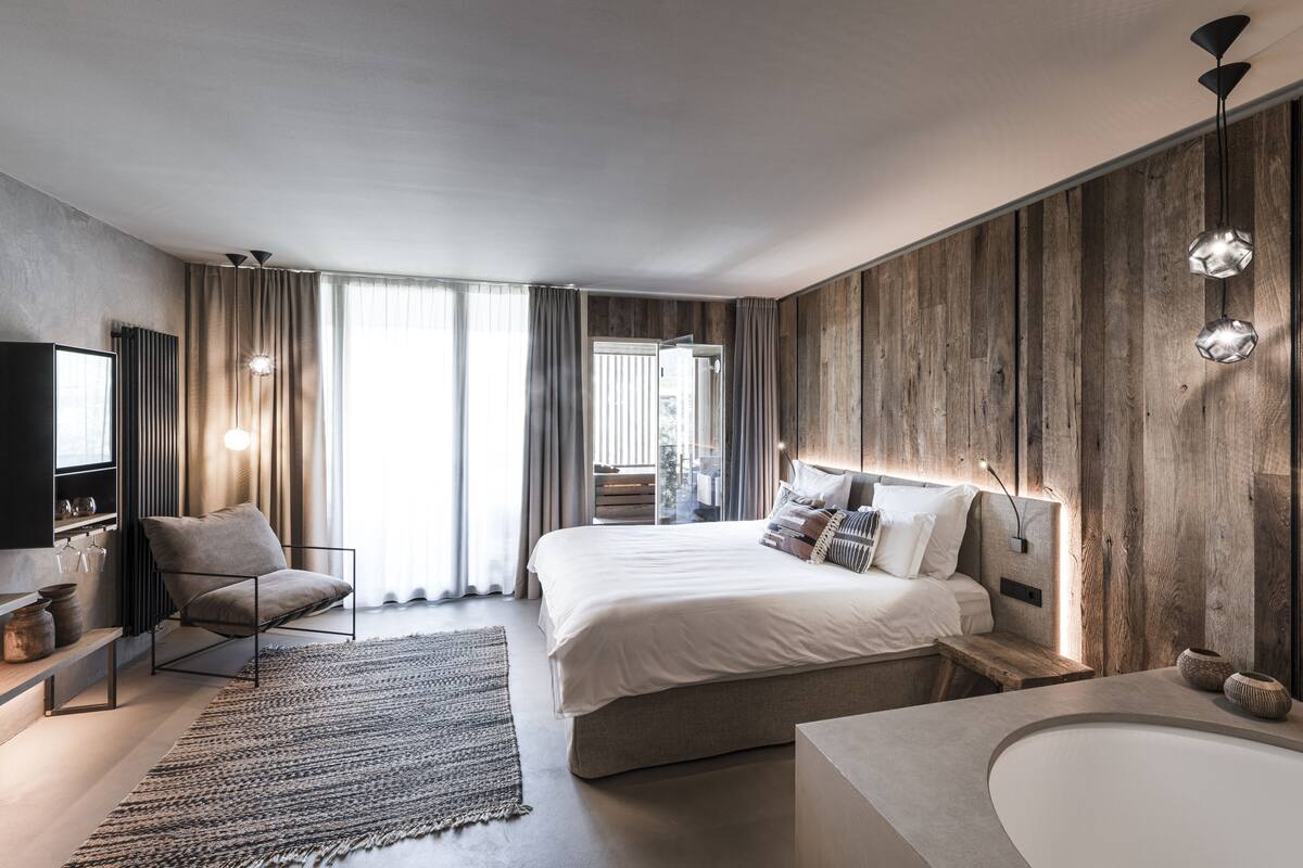 A modern hotel room with a large bed, a desk, a chair, a TV, and a bathroom with a bathtub and sink.