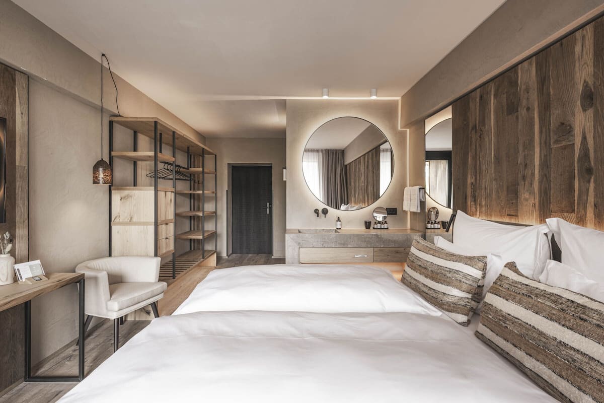 A modern bedroom with a large bed, a vanity with a mirror, a wardrobe, and a seating area with a chair.