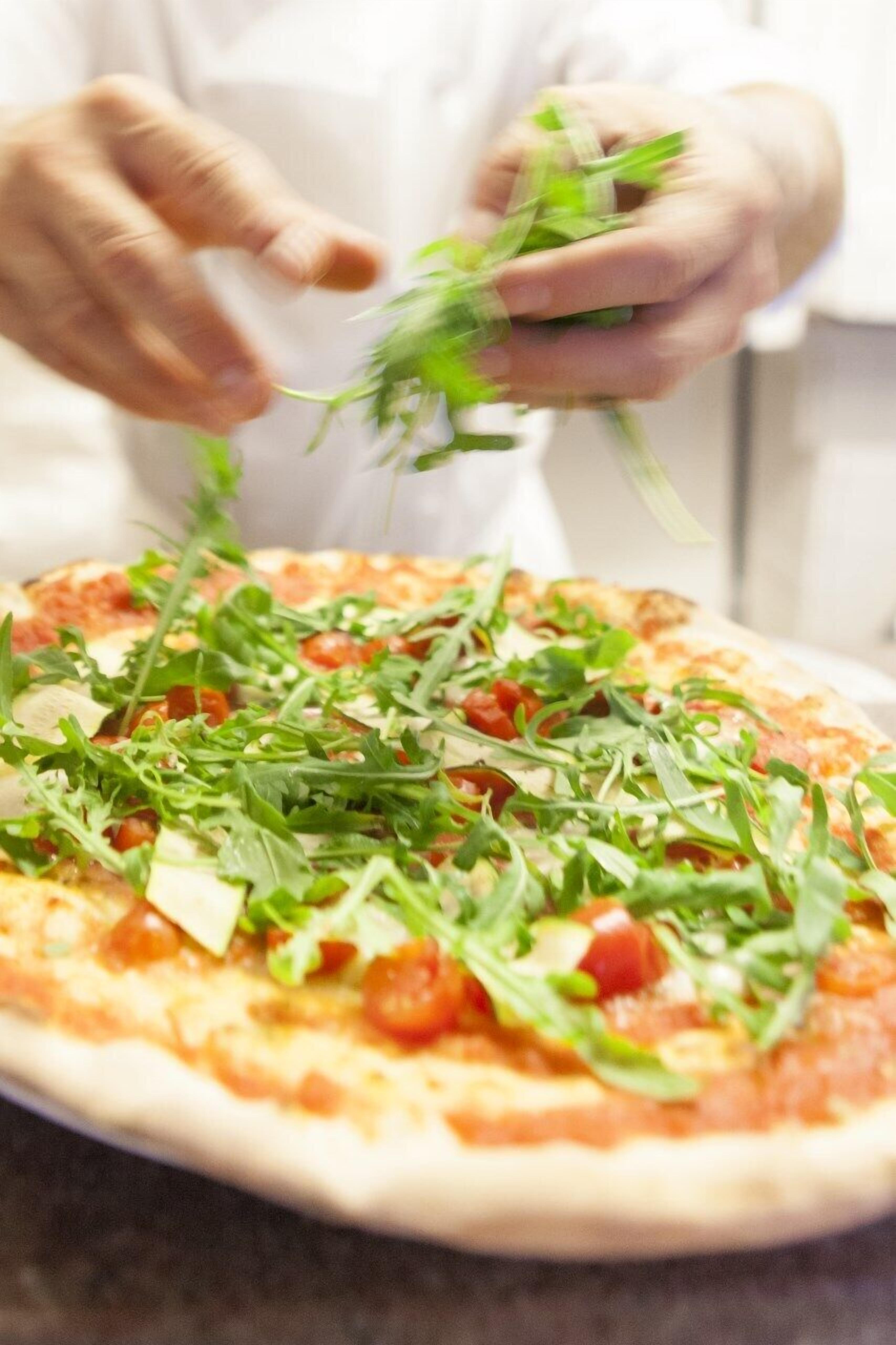A person adding fresh greens to a pizza.