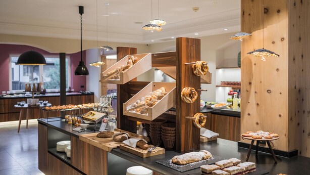 Uma área de buffet com diversos pães e doces dispostos em suportes e prateleiras de madeira.