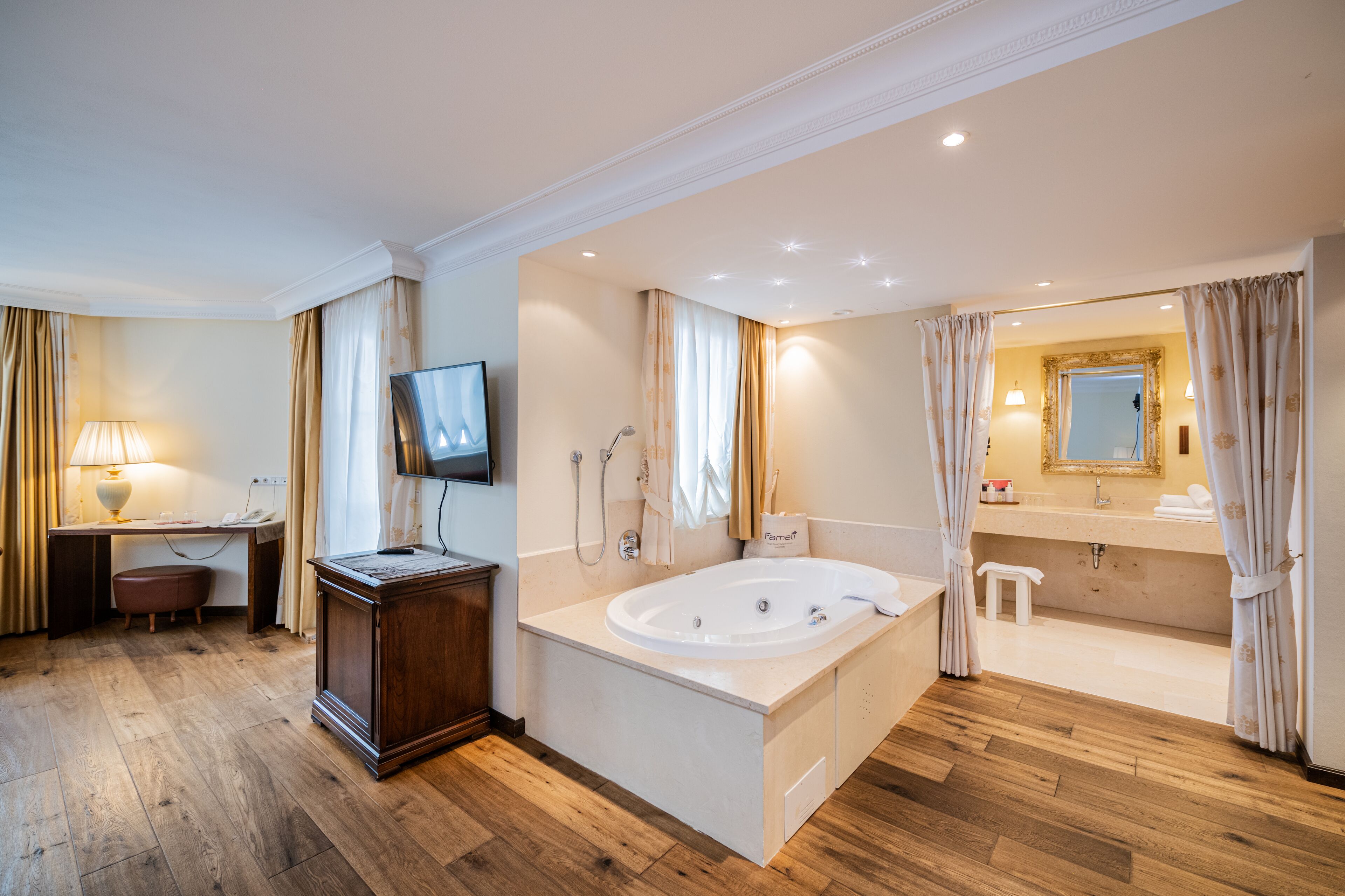 A spacious bathroom with a large bathtub, a vanity with a mirror, and a wooden floor.