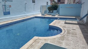 Une piscine à bord incurvé, entourée d’une terrasse carrelée et de chaises longues.