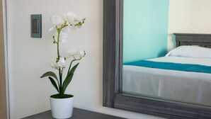 A white orchid in a white pot on a wooden nightstand, a bedside table, and a bed with a blue blanket and white pillows. - Hotel Hacienda de Castilla (Cancun)