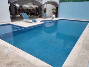 Una piscina al aire libre, sillones reclinables de piscina