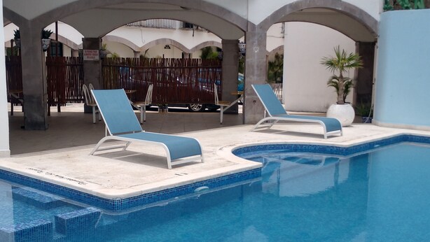 A swimming pool with two lounge chairs, a tiled deck, and a wooden fence in the background. - Hotel Hacienda de Castilla (Cancun)
