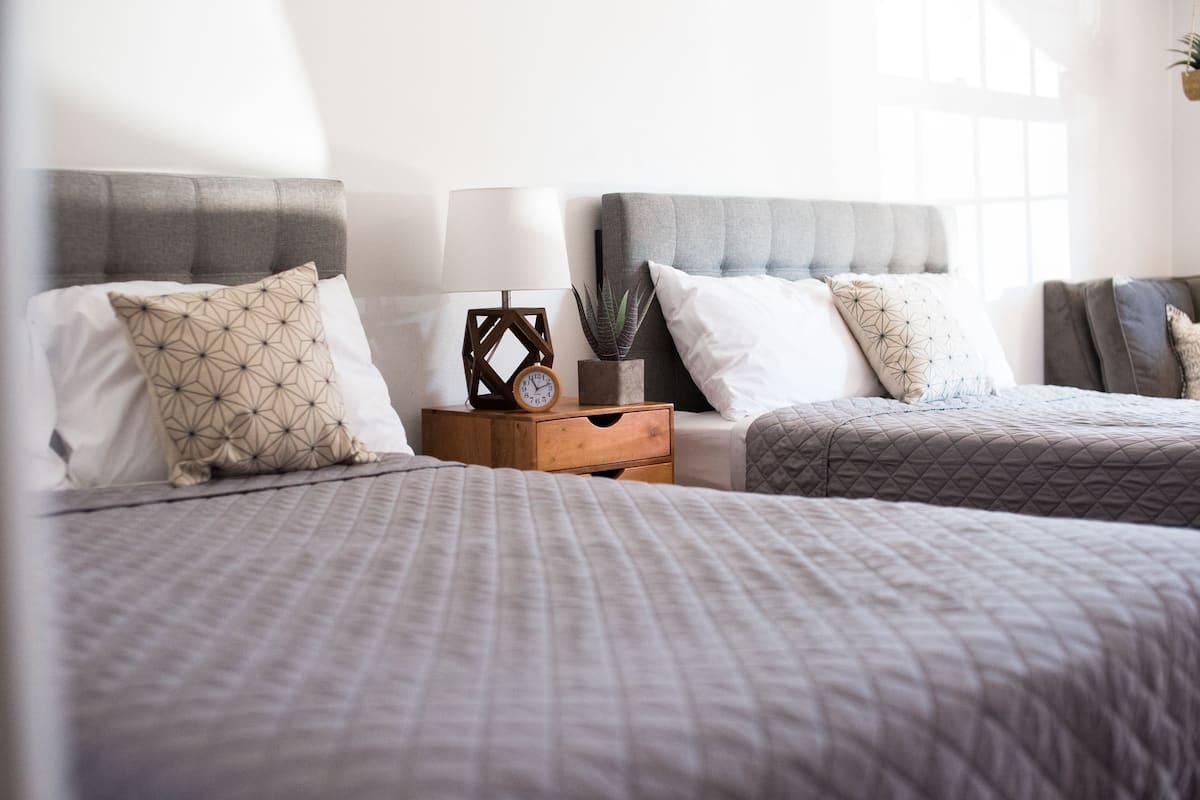 A bedroom with two beds, each with a headboard, a bedside table with a lamp, and a clock.