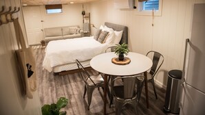 Una habitación compacta con cama, mesita de noche y un pequeño comedor con sillas y mesa.