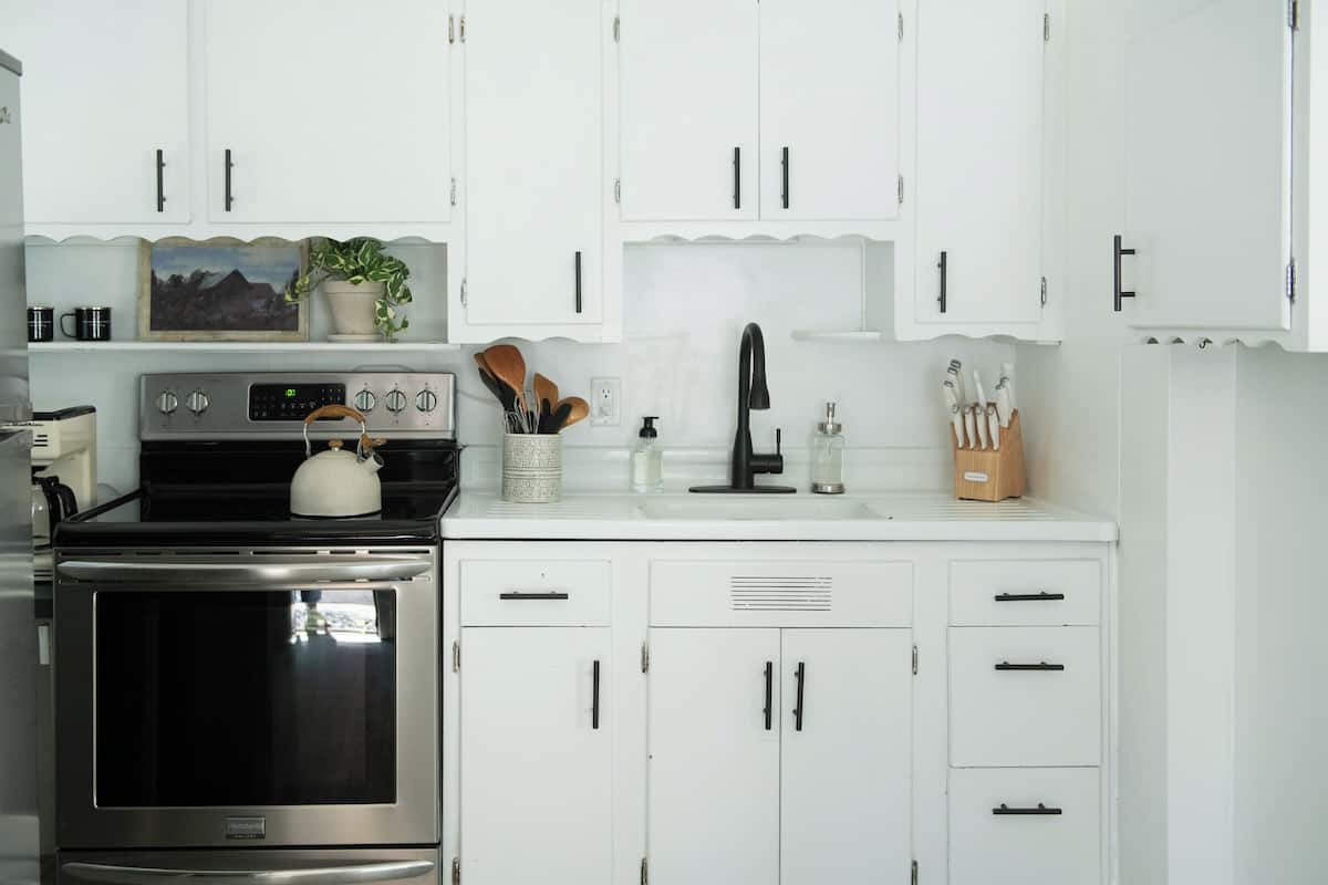 A kitchen with white cabinets, a stove, and various kitchen utensils.