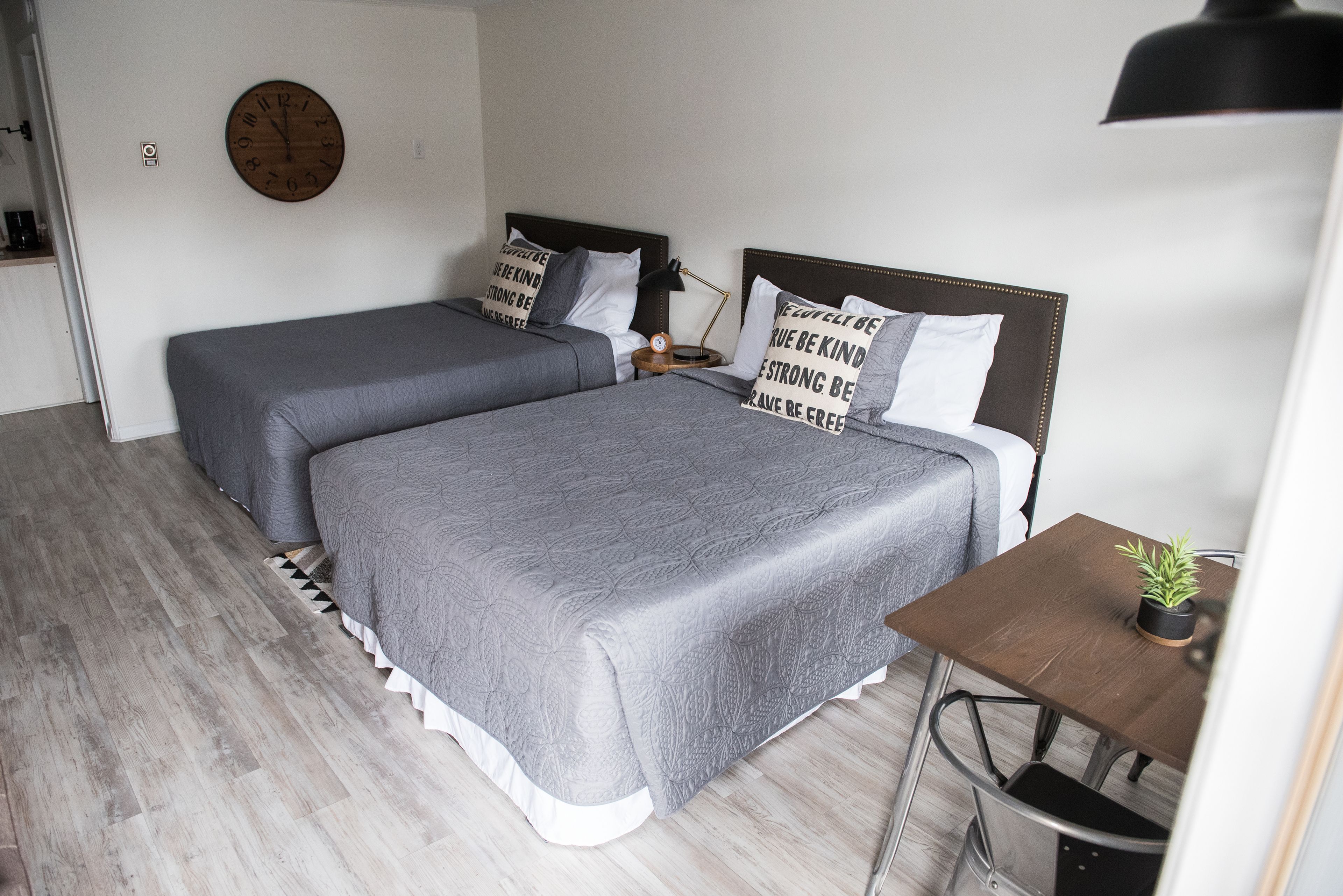 Une chambre avec deux lits, une tête de lit en bois, une table de chevet avec une lampe et une petite plante en pot.