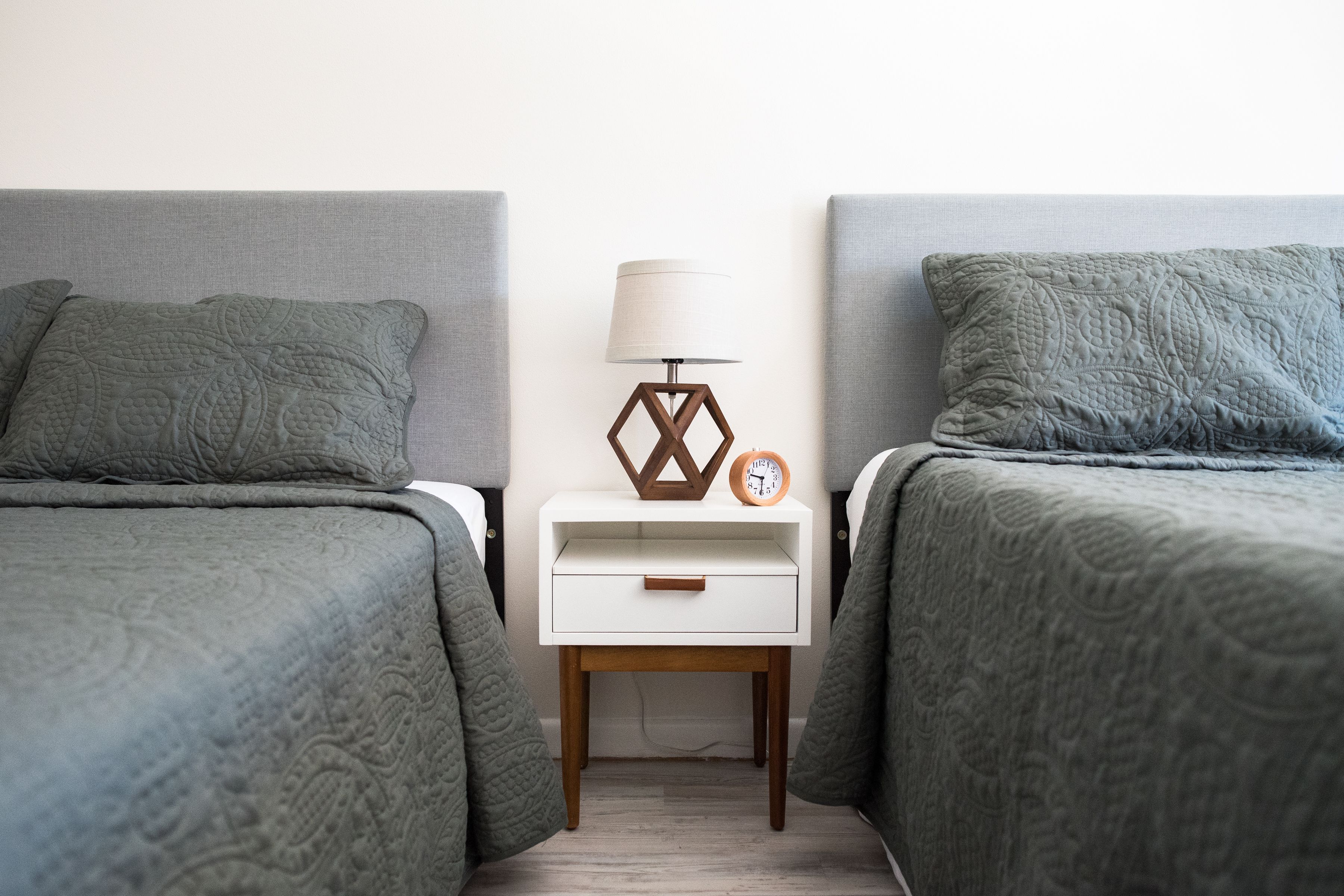 Une chambre avec deux lits, une table de chevet avec une lampe et une horloge, et un tiroir.