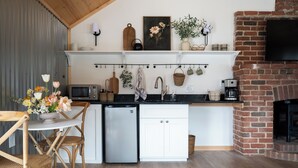Cocina compacta con refrigerador, microondas y cafetera. Hay una chimenea de ladrillo y un televisor montado en la pared.