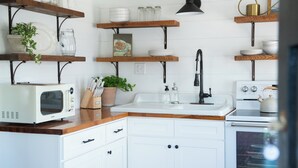 Una cocina con armarios blancos, encimeras de madera, microondas, fregadero y estufa.