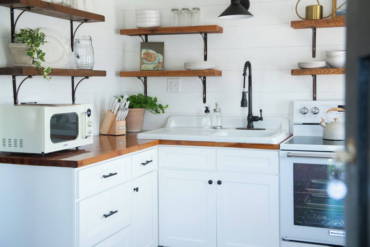 A kitchen with white cabinets, wooden countertops, a microwave, a sink, and a stove.