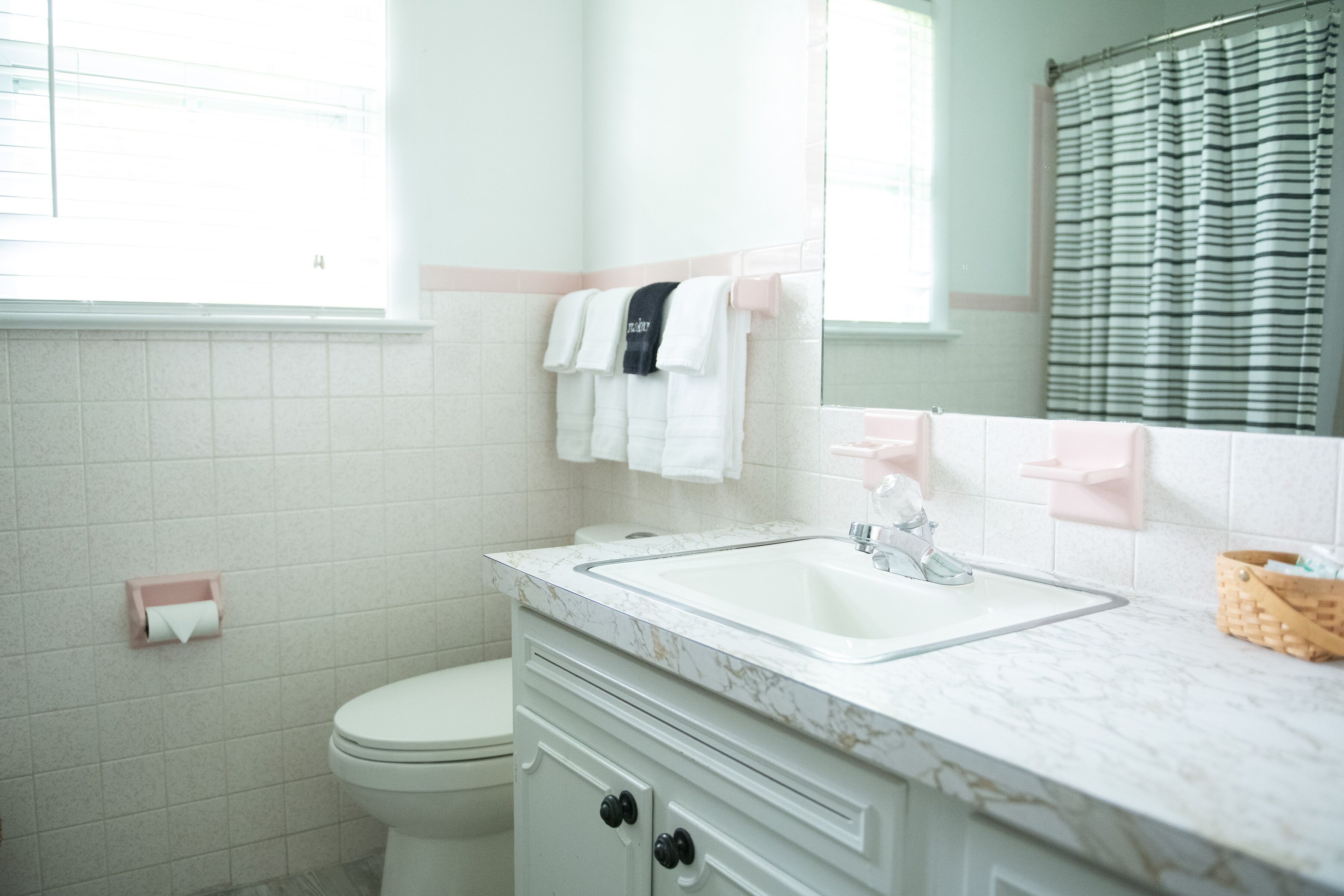 A bathroom with a white toilet, a sink with a marble countertop, a towel rack with white and black towels, and a striped shower curtain.