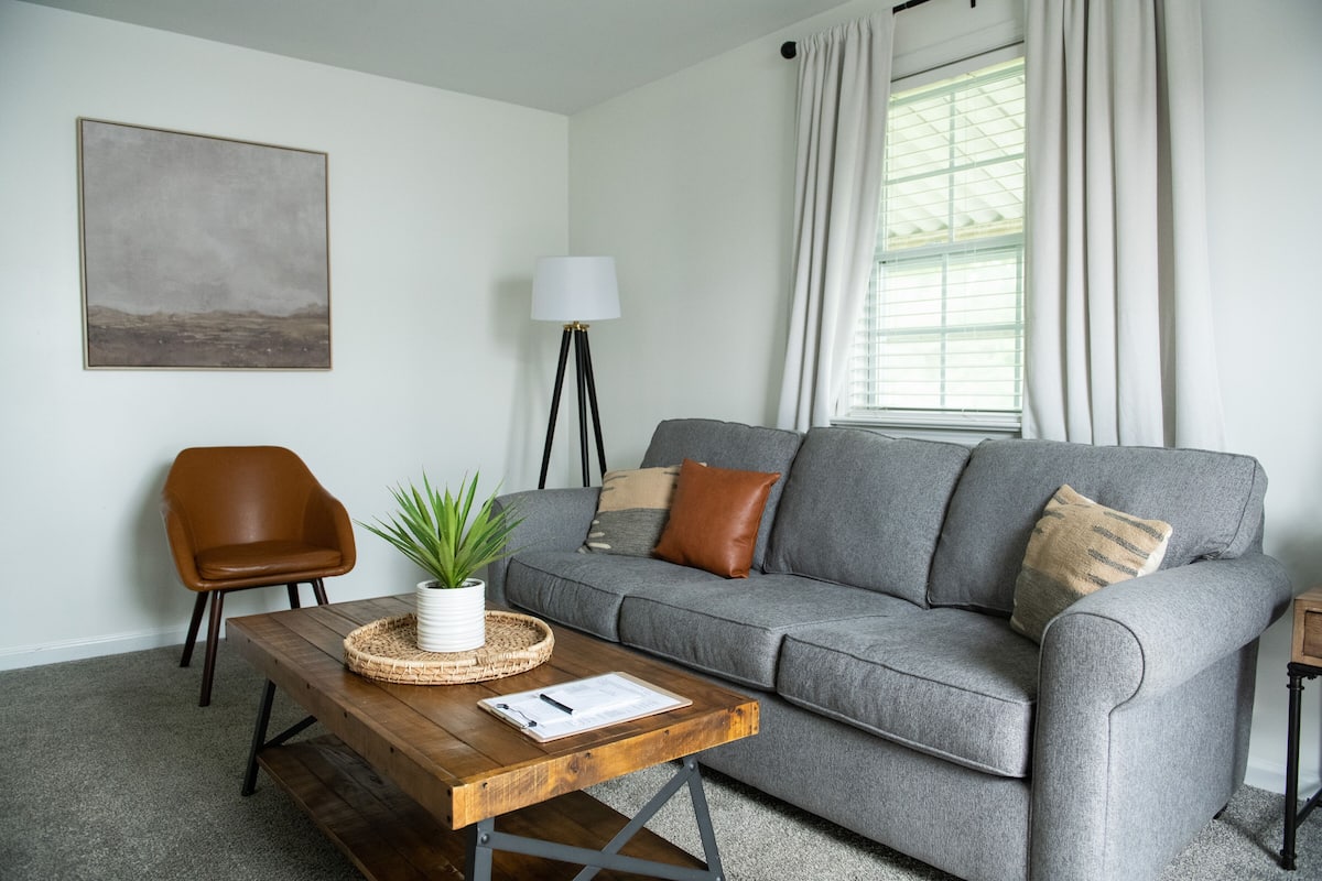 A living room with a grey sofa, brown leather chair, a wooden coffee table with a plant, and a floor lamp.