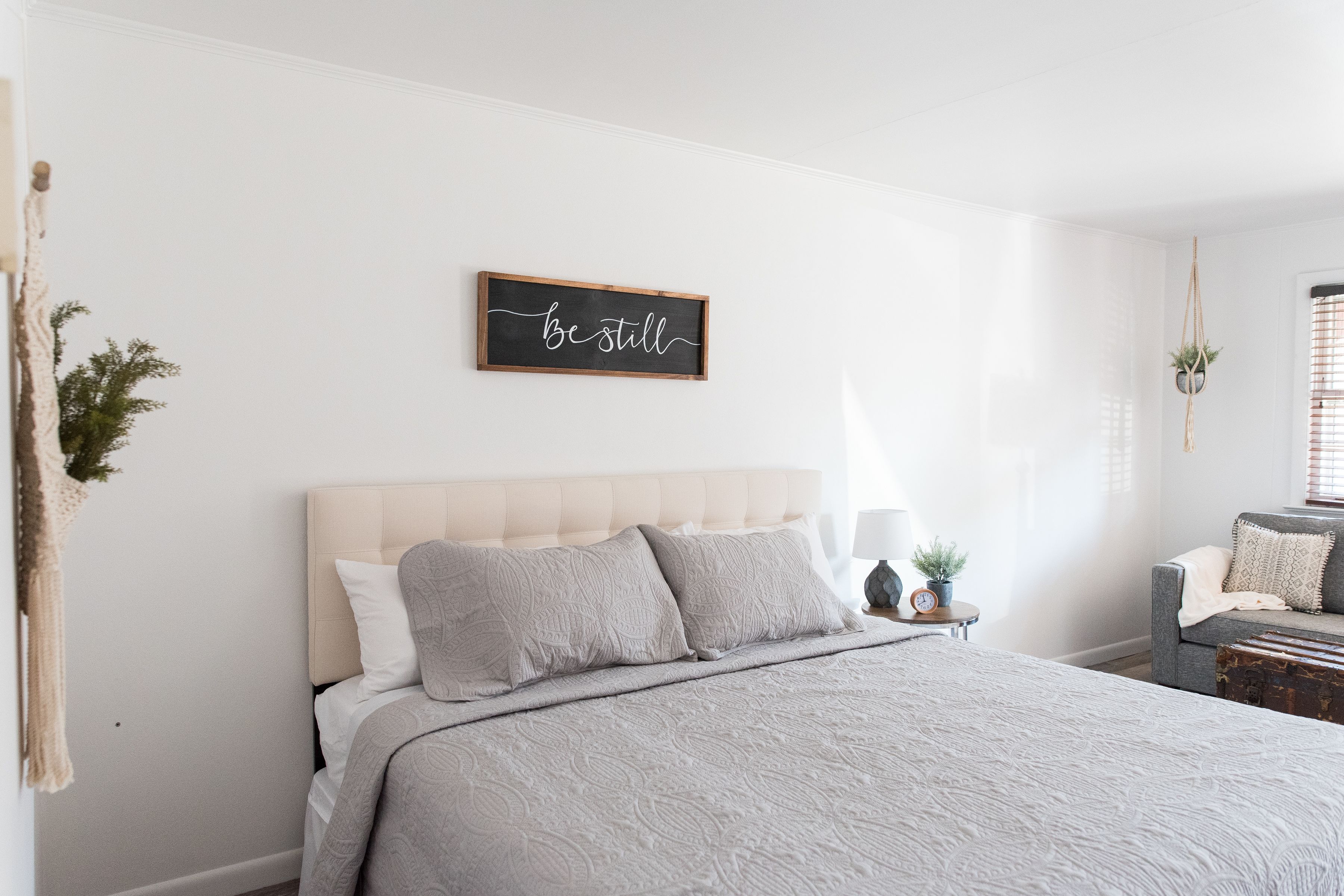 Una camera da letto con un letto, un comodino, un cartello appeso al muro e una finestra con persiane.