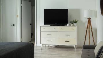 Un dormitorio con una cama, un televisor sobre una cómoda, una lámpara y una planta.
