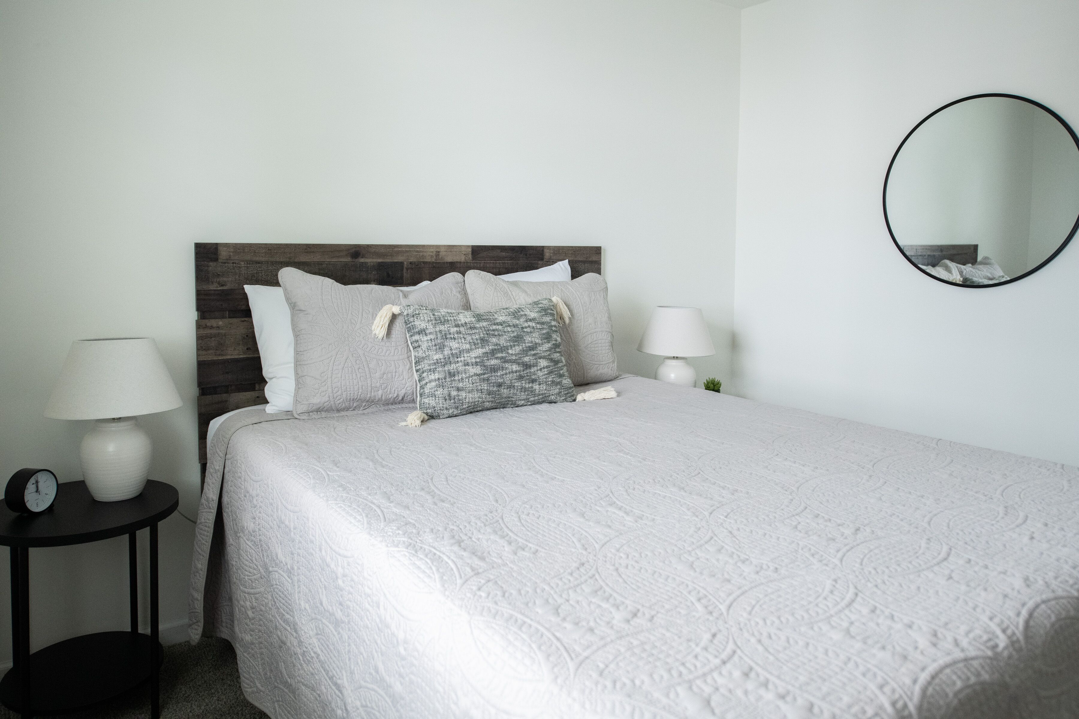 A neatly made bed with a white quilt, a wooden headboard, and two bedside lamps.