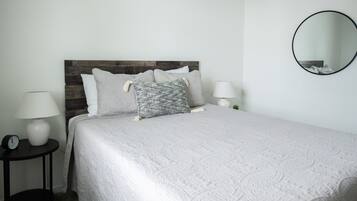 A neatly made bed with a white quilt, a wooden headboard, and two bedside lamps.