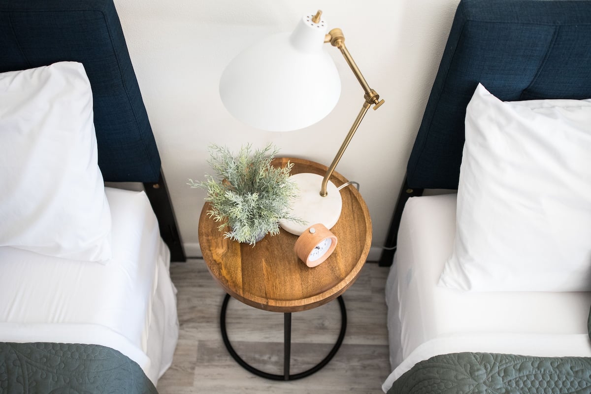 A neatly arranged bedroom with two beds, a bedside table with a lamp, and a small potted plant.