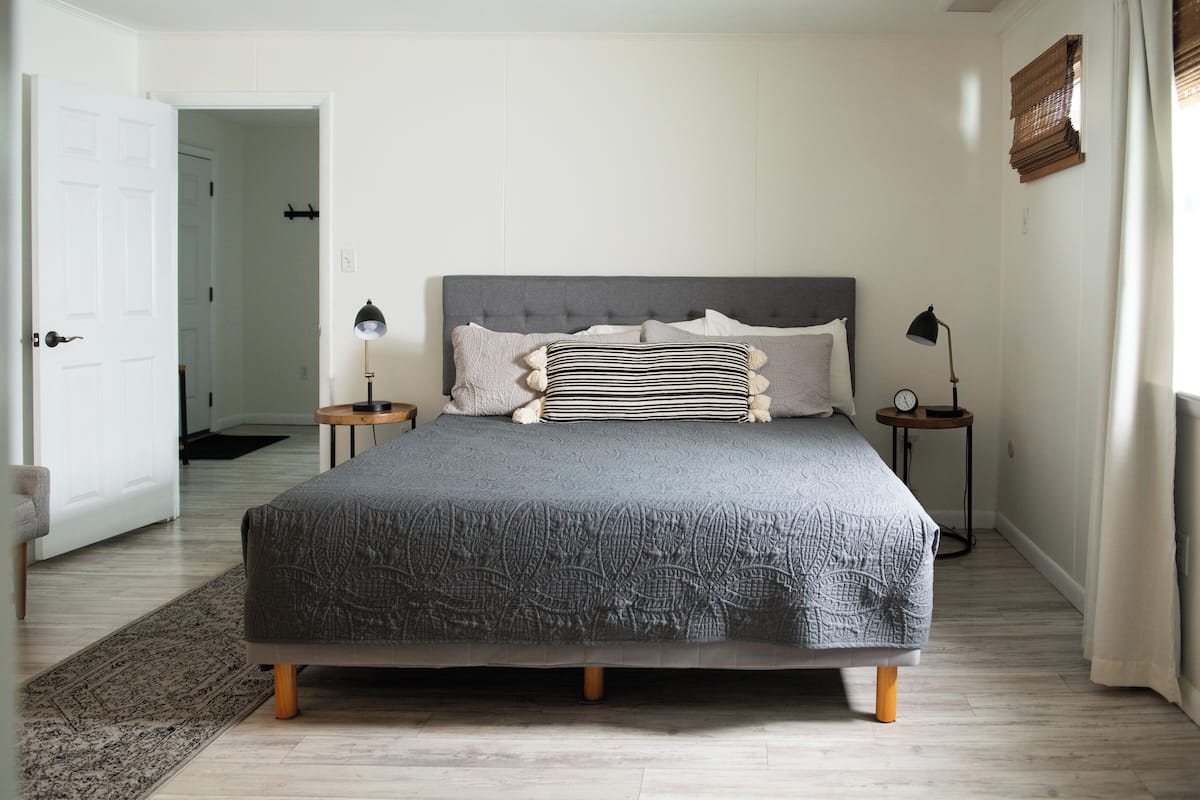 A neatly arranged bedroom with a large bed, two bedside tables with lamps, a door leading to another room, and a window with curtains.